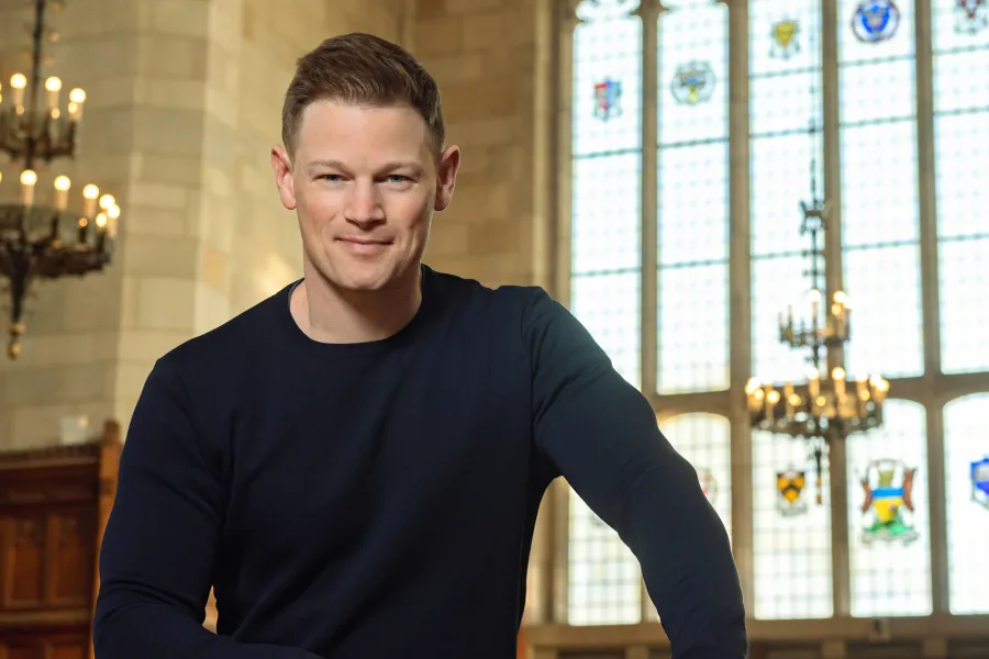 Christopher Perras, standing in front of the window in the University of Michigan law library