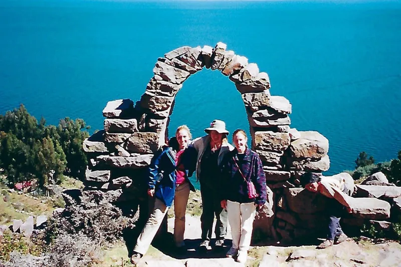 A portrait of Kirsten Matoy Carlson, ’03 and other people posing in front of a stone arch.