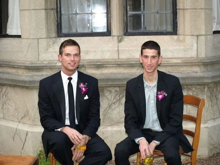 Two men in suits sit knee-to-knee in front of a Lawyers Club window.