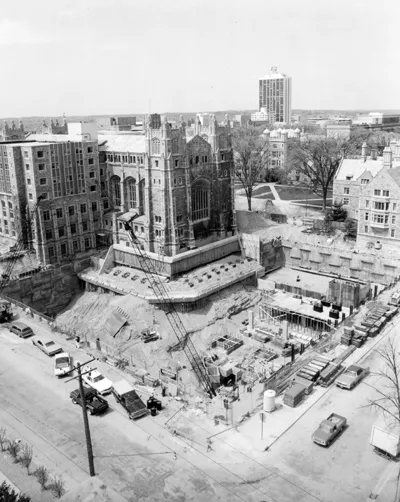An open pit surrounded by construction equipment is visible in front of the Michigan Law Quad.