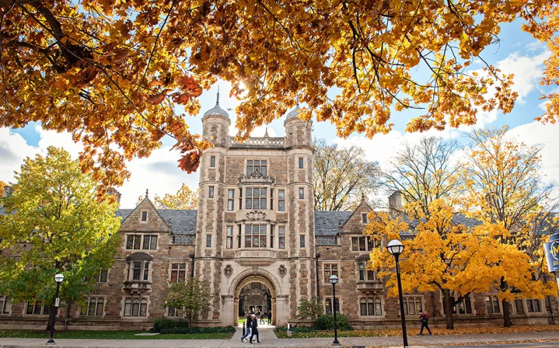 A student walks in front of the Lawyers Club in the warm autumn light.