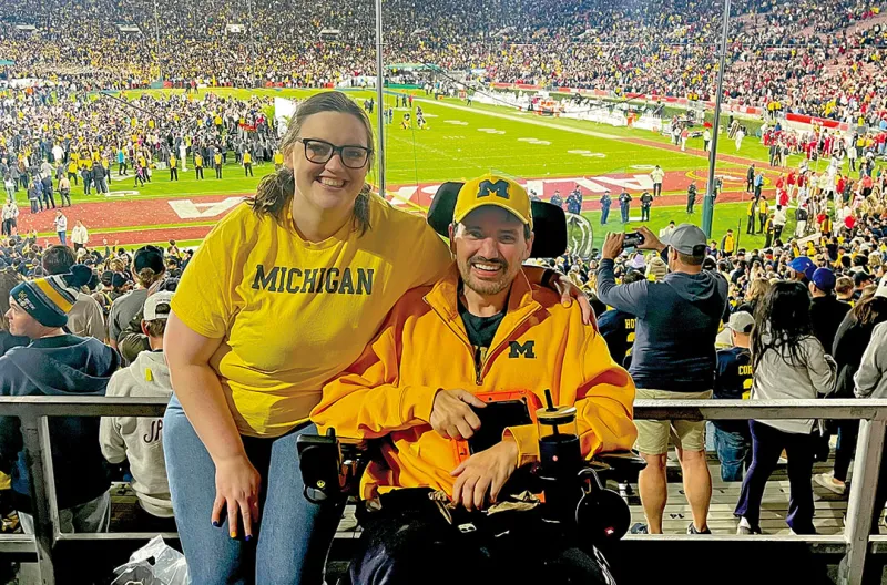 Two people standing in a stadium during a Michigan Wolverines football game.
