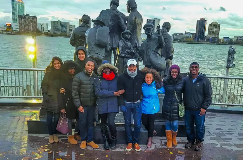 A group of people pose in front of a statue near a water front.