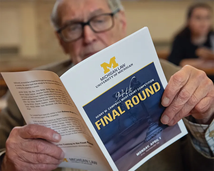 summer-2025-cover-feature-aside-008.jpg A man reads a program that has the University of Michigan logo and the text "FINAL ROUND" on the cover.