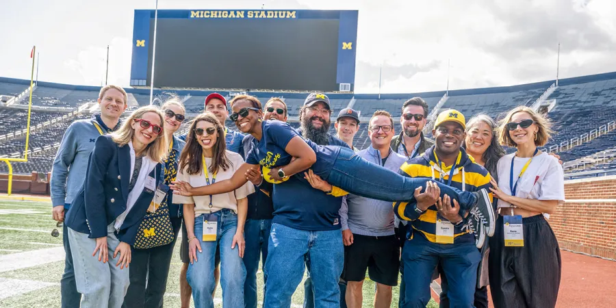 Ashley M. Washington (aloft), ’10, with classmates during a 2025 Reunion event at Michigan Stadium.