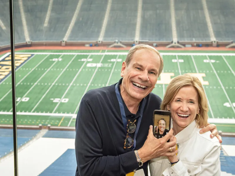 Two people smiling with the football stadium in the background
