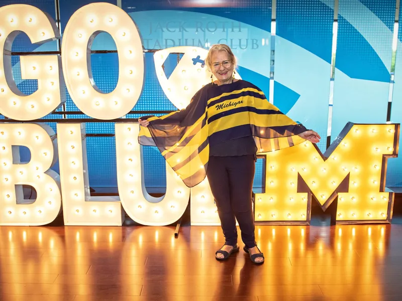 A person standing in front of a big illuminated Go Blue sign