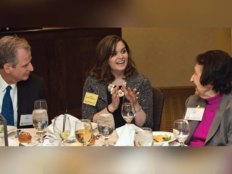Three people around a table, talking joyously at a Law School event.