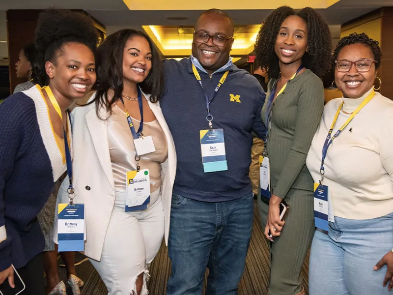 A group of people gathering and smilingPeople gathering, and smiling inside at the UM Bar Alumni Reception at the Big House