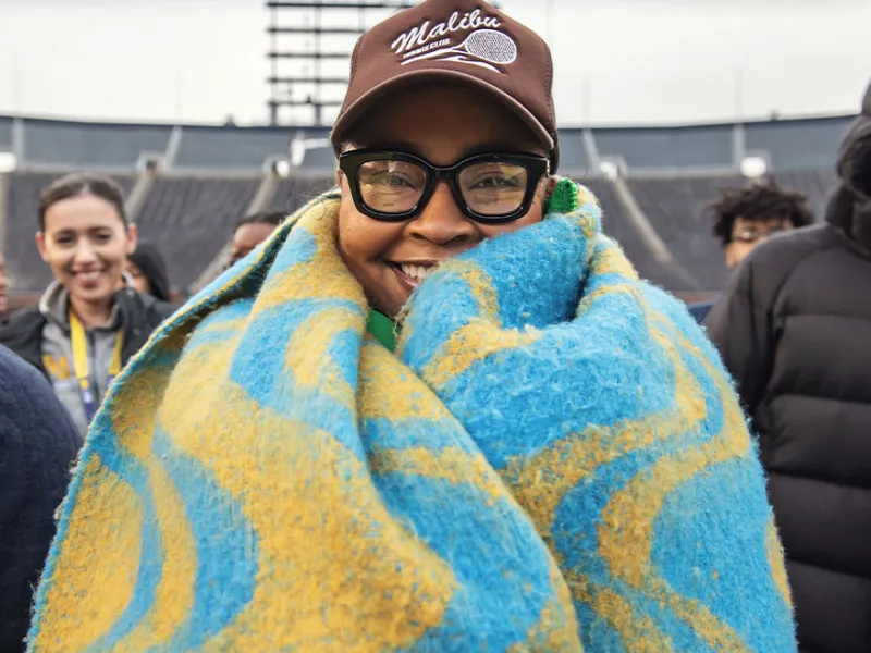A woman wrapped in a blanket, smiling at the UM Bar Alumni Reception at the Big House