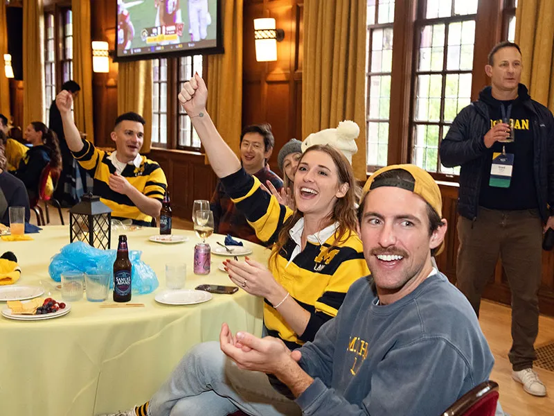 Student sitting at a table cheering while watching football game.