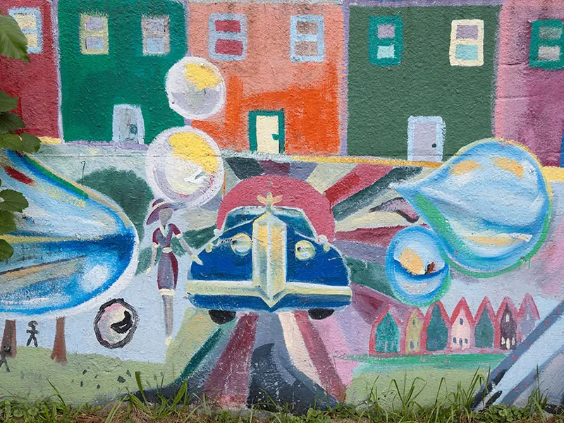 A mural of a car in front of buildings.