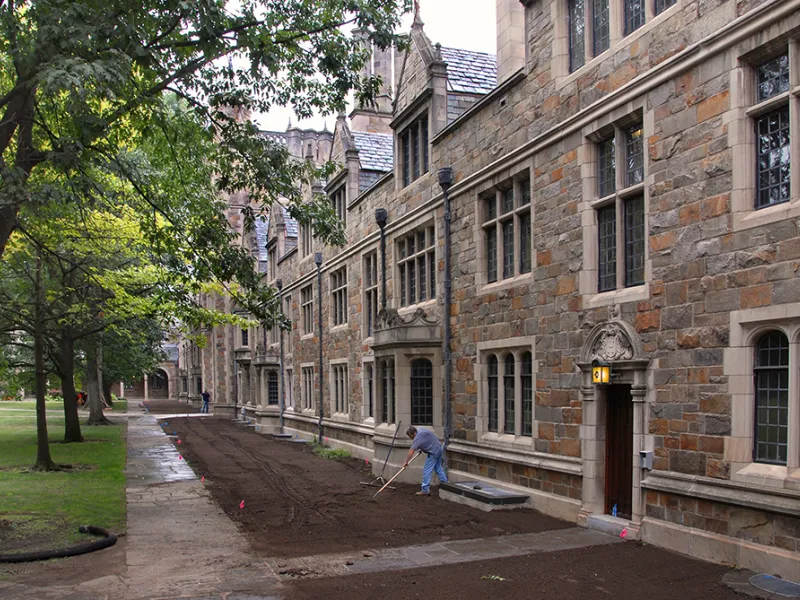 A gardener smooths mulch and soil next to the completed and renovated Lawyers Club.