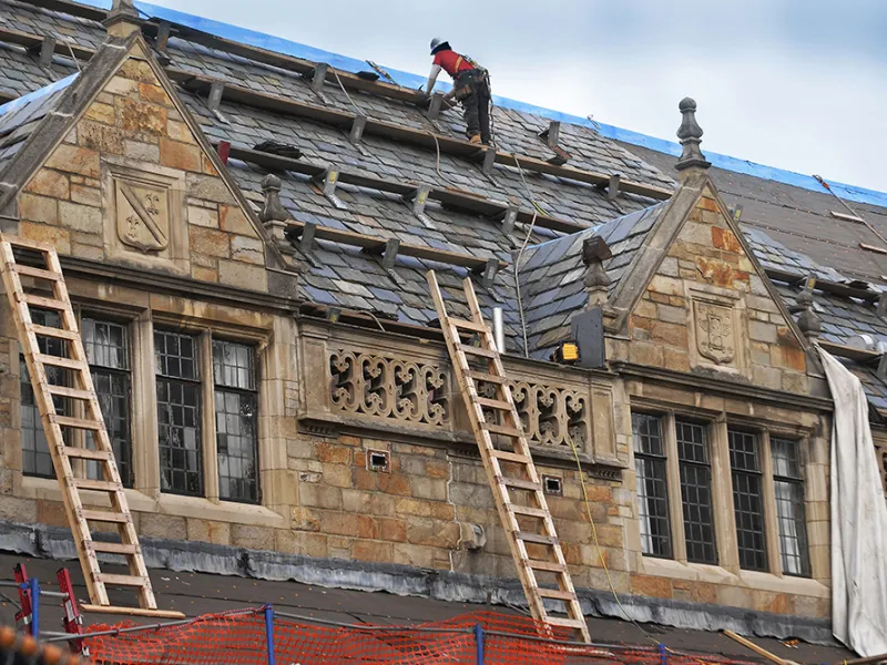 A construction worker examines the Lawyers Club roof while balanced on a wooden walkway.
