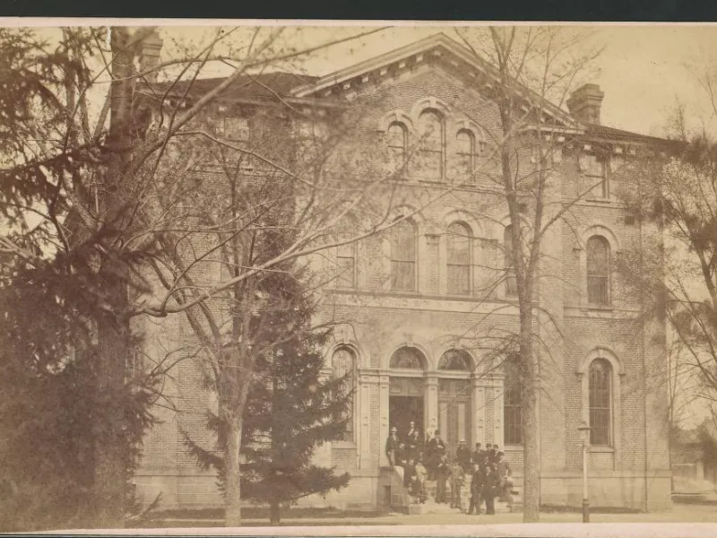 The original Law Building stands behind a thin copse of trees.