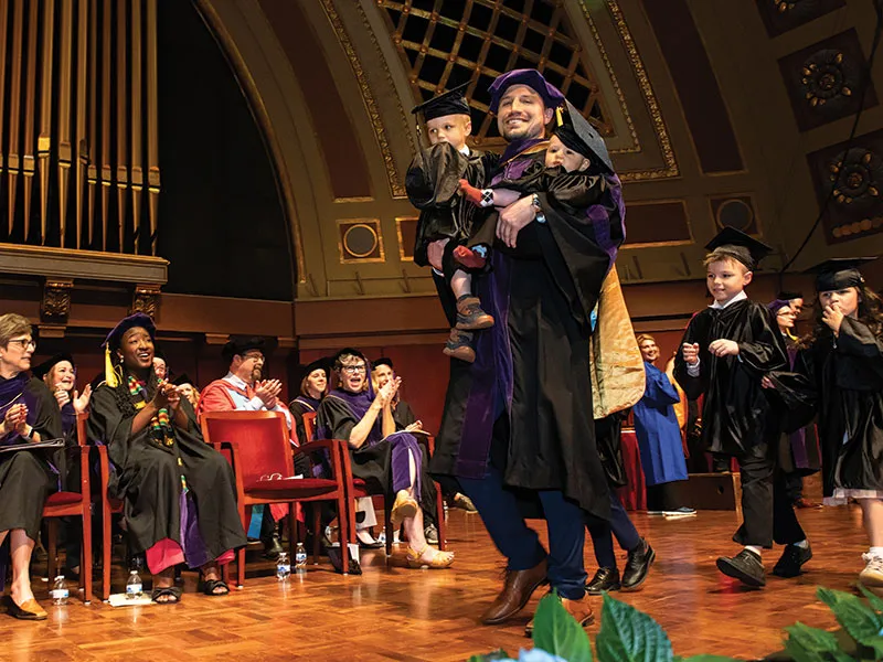 A Michigan Law graduate walks across stage with their children.