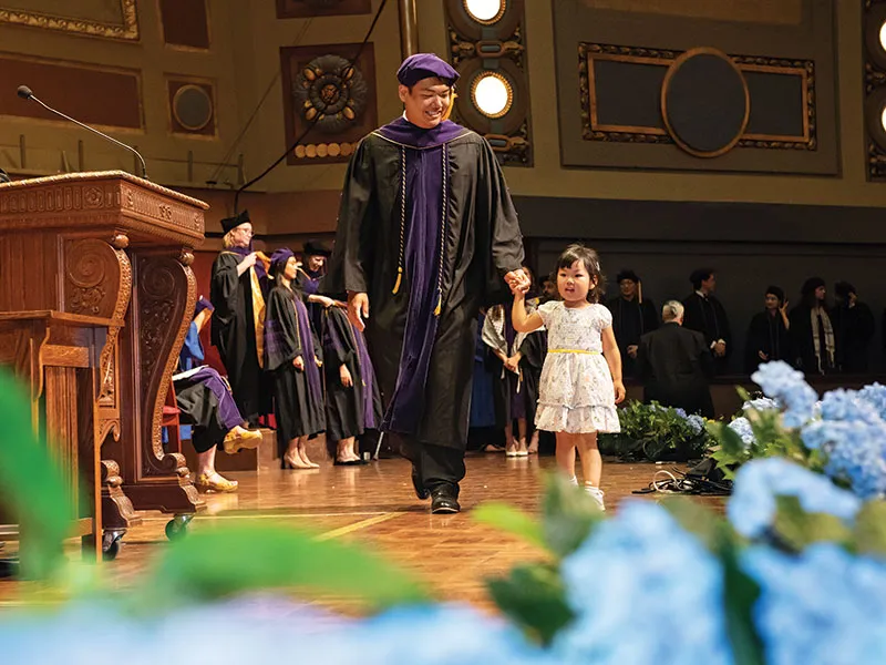 A Michigan Law graduate walks across stage with their child.