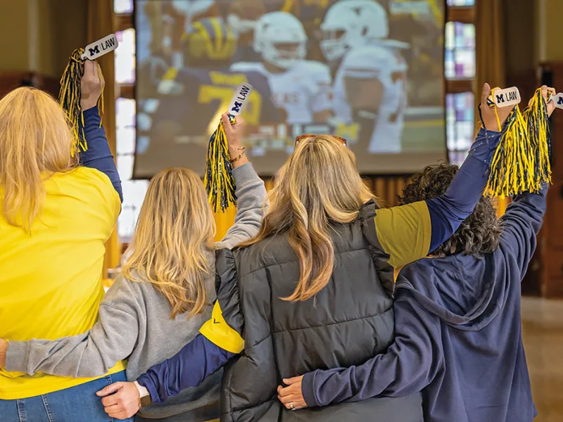 Michigan Law alumni gather for a reunion in the Lawyer's Club lounge watching a football game..