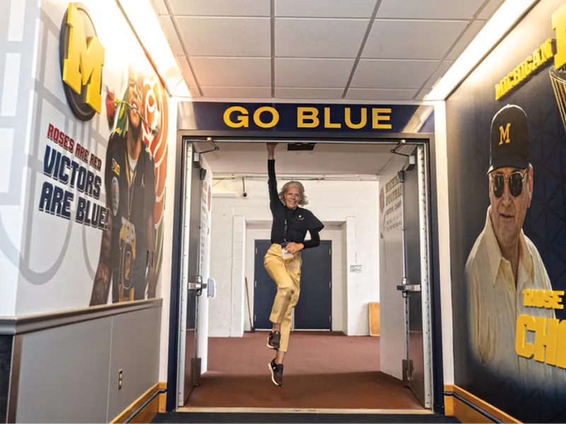 Michigan Law alumni jumps and taps a Go Blue sign