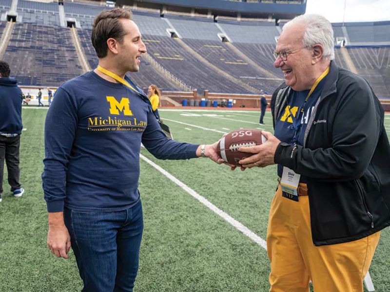 Two Michigan Law alumni pass along a football