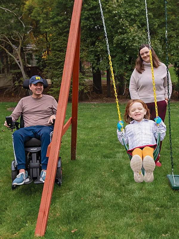Two people pushing a child on a swing.