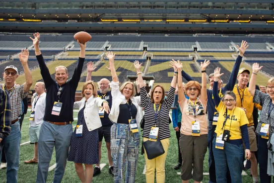 People waving their hands excitedly in the Michigan Big Ten football stadium enjoying a reunion gathering