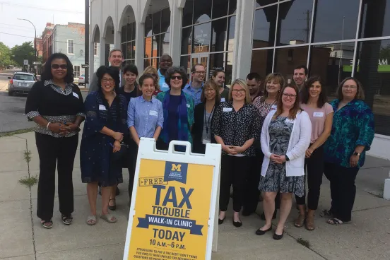 A group of people from the Michigan Law School Tax Clinic smiling and standing together feeling proud of the work they are accomplishing.  