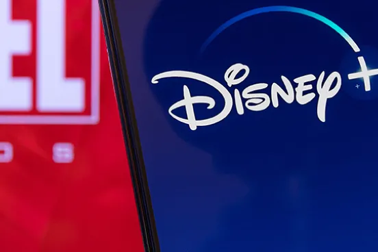 An iPhone shows the Disney Plus app in front of the Marvel logo.