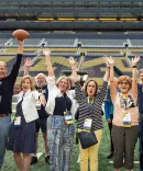 People waving their hands excitedly in the Michigan Big Ten football stadium enjoying a reunion gathering