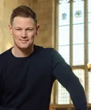 Christopher Perras, standing in front of the window in the University of Michigan law library