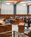 A mock trial being held at Michigan Law A courtroom scene shows a judge presiding over a case, with a lawyer presenting evidence to an attentive audience in a wooden-paneled space.