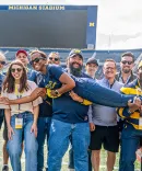 Ashley M. Washington (aloft), ’10, with classmates during a 2025 Reunion event at Michigan Stadium.